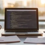 Modern ofiste JavaScript kodu üzerinde çalışan profesyonelin düzenli masasında dizüstü bilgisayar, notlar ve kahve fincanı.